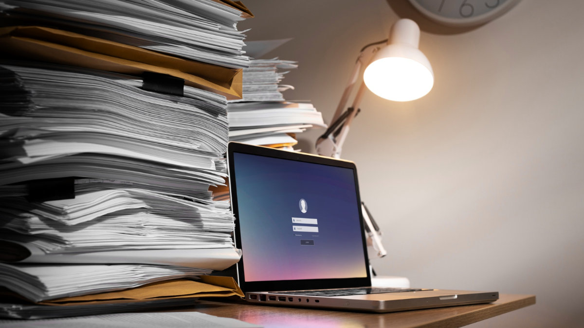 Folders on a desk with a laptop in front of them showing a login screen