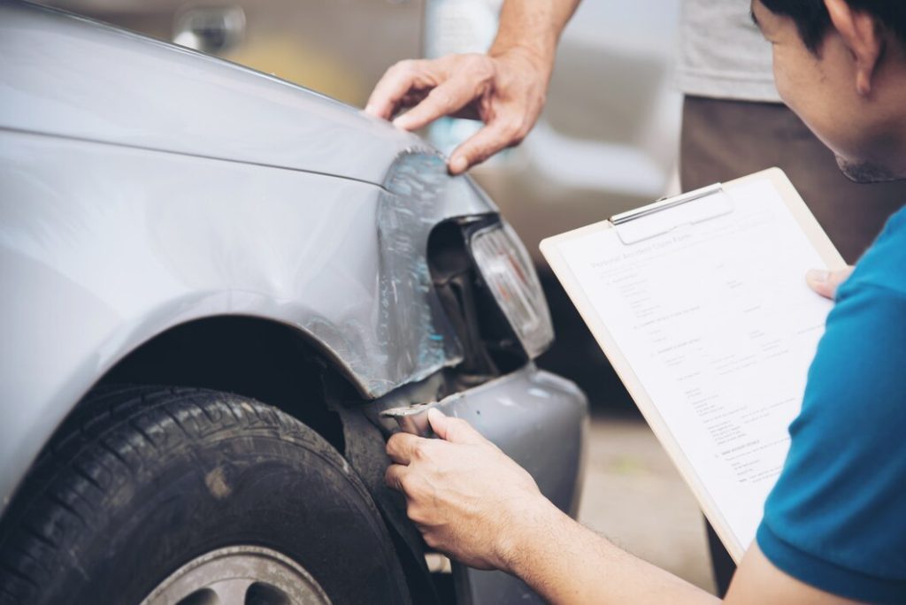 A person with a clipboard inspecting the dented around the headlight on a car